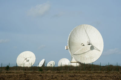 Parabolic satellites on field against sky