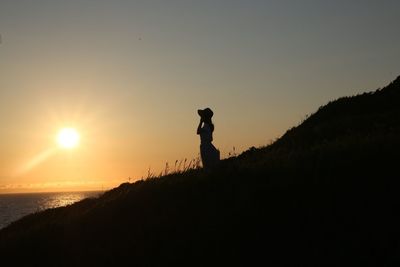 Silhouette woman standing on coast against clear sky during sunset