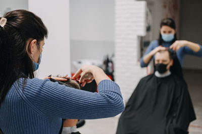 Close-up of female barber in mask cutting hair of man in salon