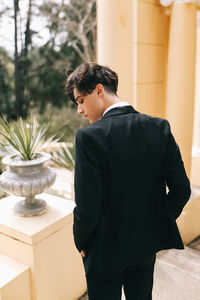 A beautiful young man, the groom in an elegant wedding suit, stands posing in the city's old park