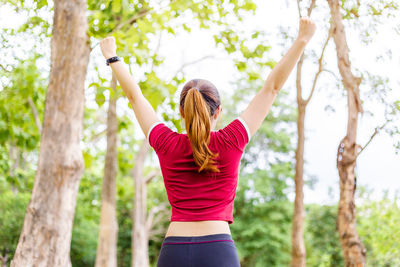 Rear view of woman with arms raised in forest