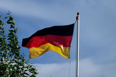 Low angle view of german flag waving by branch against blue sky