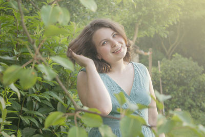 Portrait of smiling young woman standing by plants in park