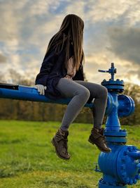Full length of woman sitting on pipe against cloudy sky