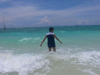 Rear view of man standing on beach against sky