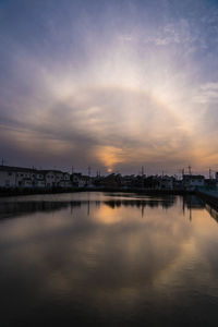 Scenic view of river by buildings against sky during sunset