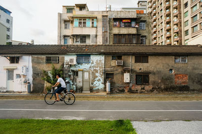 Man riding bicycle on road by buildings in city