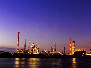 Illuminated factory by sea against clear sky at night