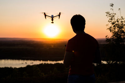 Rear view of silhouette man standing by airplane against sky during sunset