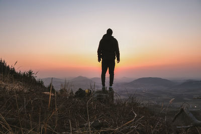 Rear view of silhouette man standing on mountain against sky during sunset
