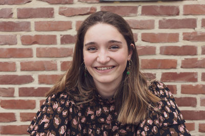 Close up shot of a beautiful brown haired teenager smiling, against a red brick background