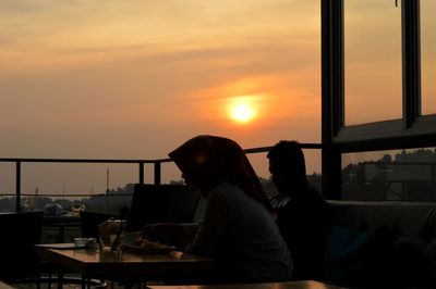 People sitting in city against sky during sunset