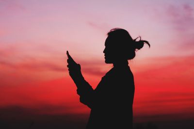 Silhouette woman using phone against dramatic sky