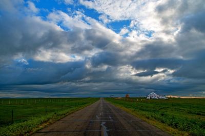 Road passing through landscape against storm clouds