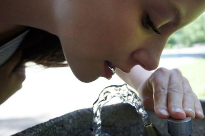 Close-up of young woman drinking water though faucet in park