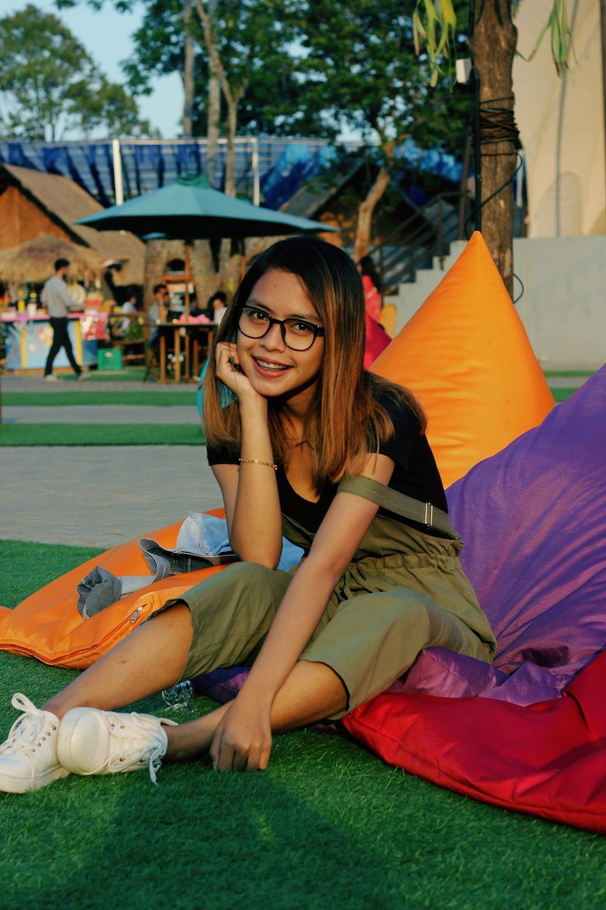 FULL LENGTH OF A SMILING YOUNG WOMAN SITTING AGAINST BLUE WALL