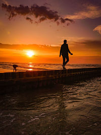 Silhouette man standing on beach against sky during sunset