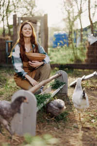 Portrait of young woman feeding chickens at farm