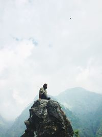 Man sitting on rock formation against mountains and sky