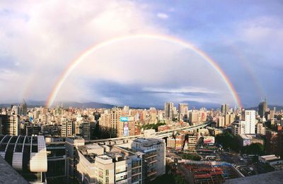 Rainbow over buildings in city against sky