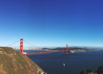 View of suspension bridge over river against blue sky