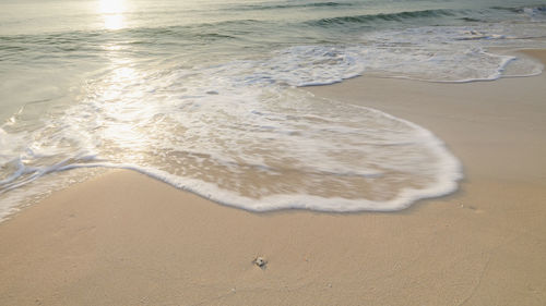 Long exposure shot sandy beach and the sea wave white bubbles with the sunrise background