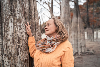 Portrait of woman standing by tree trunk in forest