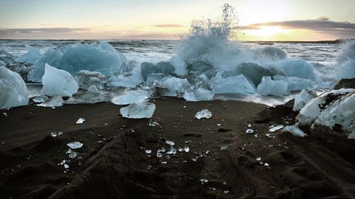 Close-up of waves splashing on beach against sky during sunset