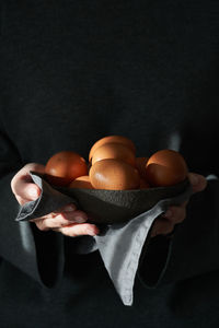 Unusual easter on a dark background. a bowl of brown eggs with hands. darkness, rays of sunlight 