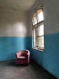 Interior of abandoned building with pink armchair and big window.