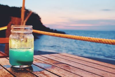 Close-up of drink on table against sea during sunset