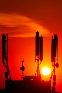 Silhouette of communications tower against orange sky