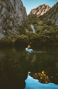 Rear view of woman canoeing on lake against mountains in forest