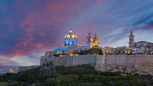 Illuminated buildings against sky at dusk