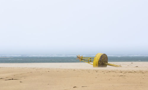 Rear view of woman sitting on beach against clear sky