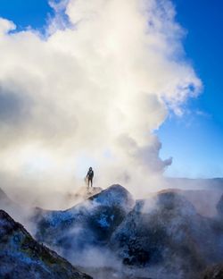 Man standing on rock formation against cloudy sky