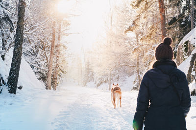 Rear view of man with dog walking in snow