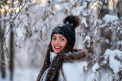 Portrait of smiling young woman standing against trees during winter
