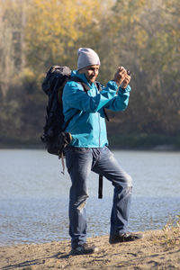 Portrait of traveler man at lake in autumn makin a photo 