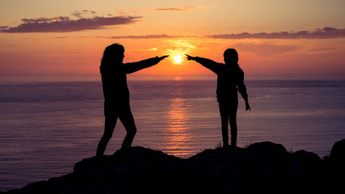 Silhouette people standing on rock at beach during sunset