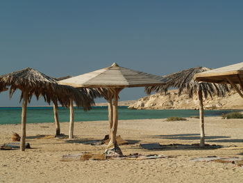 Parasols at sandy beach against clear sky