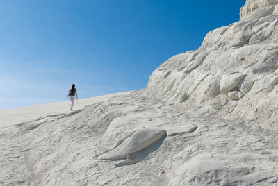 Rear view of woman walking on scala dei turchi against clear blue sky