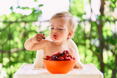 Baby girl sitting while eating strawberry at home