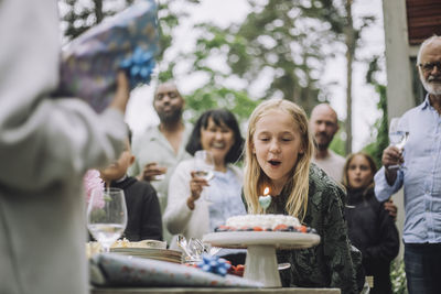 Happy girl blowing candle on cake during birthday celebration with family