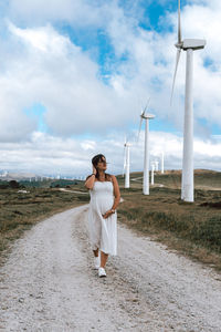 Full length of woman walking on dirt road against cloudy sky