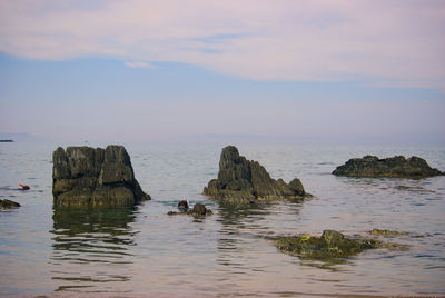 Rocks in sea against sky during sunset