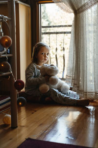 Child sitting on the floor and playing ant home. dreamy sunny mood. girl looking though the window