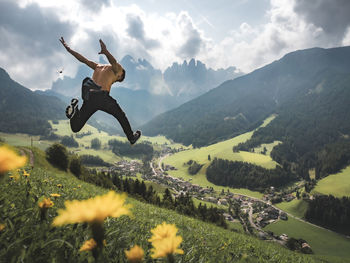 Rear view full length of shirtless man jumping on mountain at town