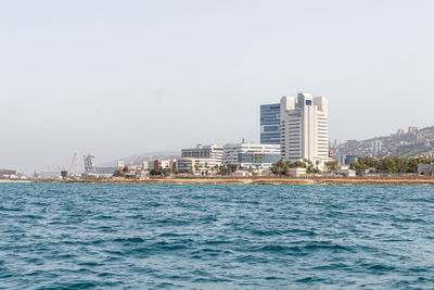 Sea by buildings against clear sky