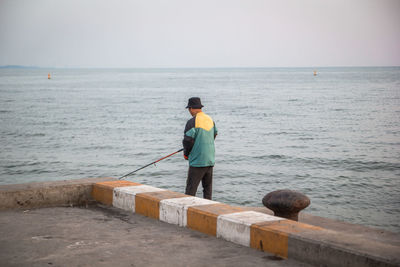 Rear view of man fishing by sea against sky